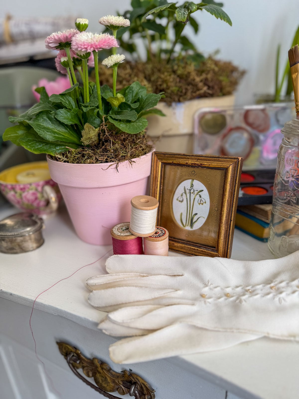 White cotton gloves, vintage thread spools and a gold framed botanical print representing Meg March at a Little Women party.