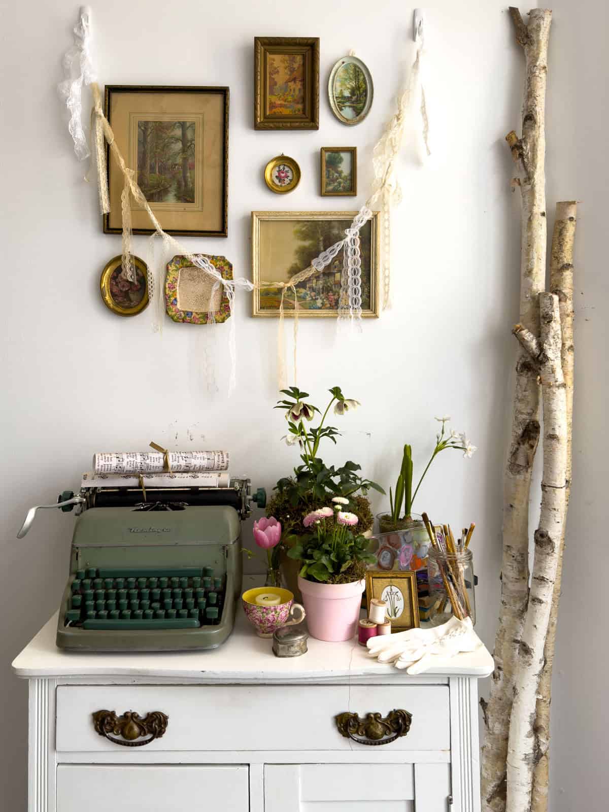 White vintage dresser styled with a green typewriter, flowers, watercolors, gloves and lace garland for a Little Women party.