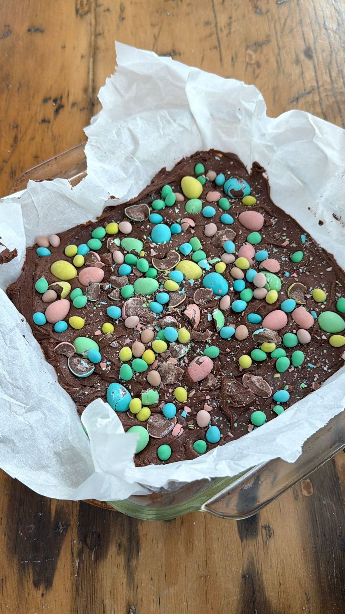 Cadbury mini egg brownies with chocolate frosting topped with pastel mini eggs in a parchment lined pan.