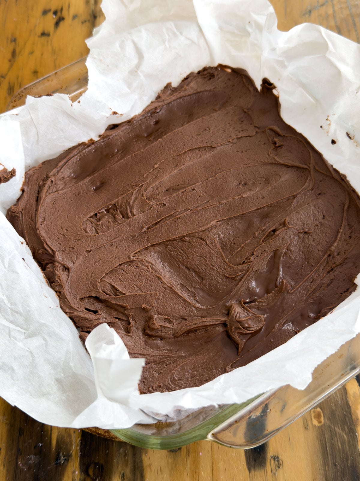 Chocolate frosting spread over warm mini egg brownies in a parchment lined pan.