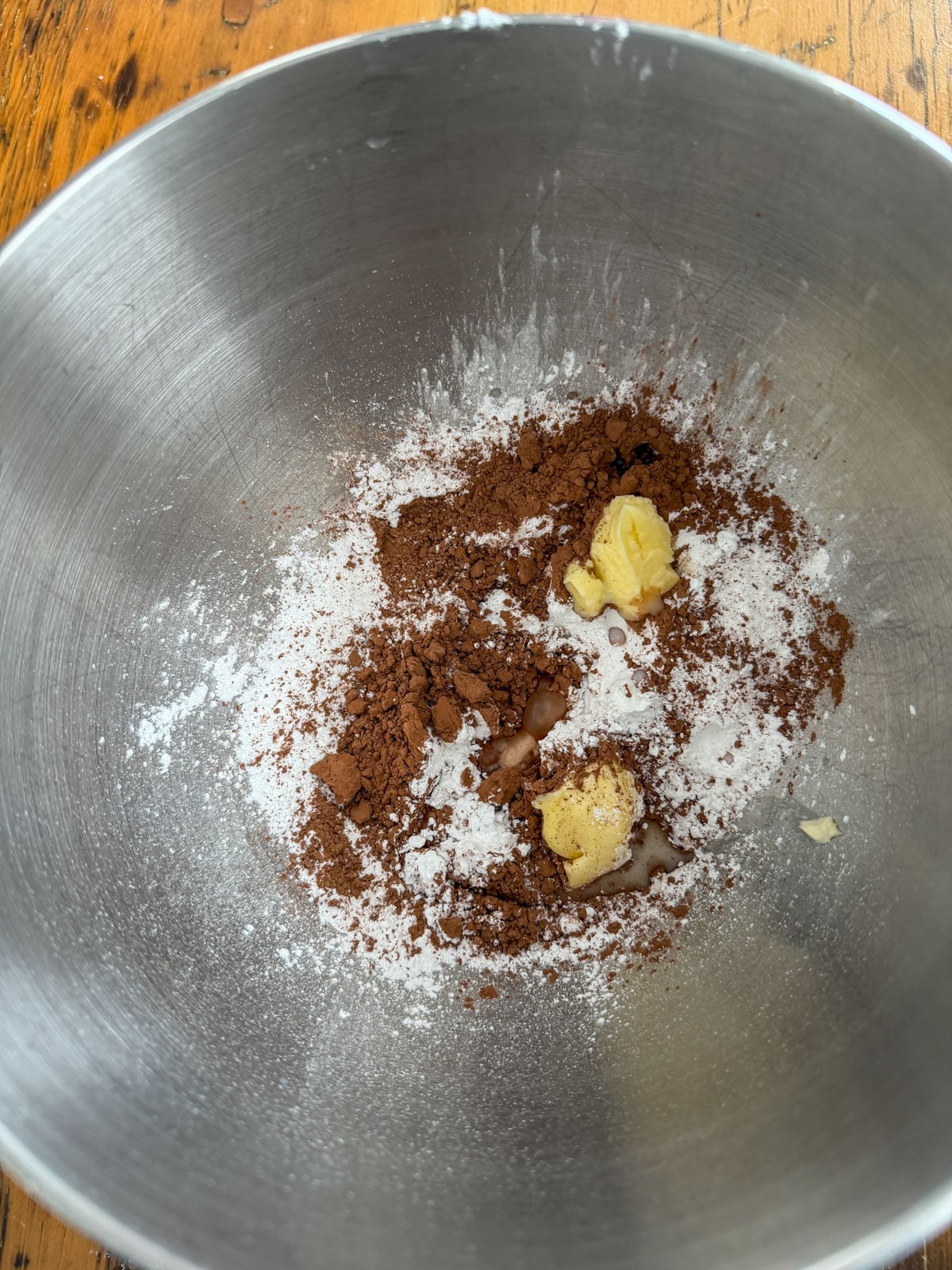 Chocolate frosting ingredients including powdered sugar, cocoa powder, butter and milk in a silver mixing bowl before combining.