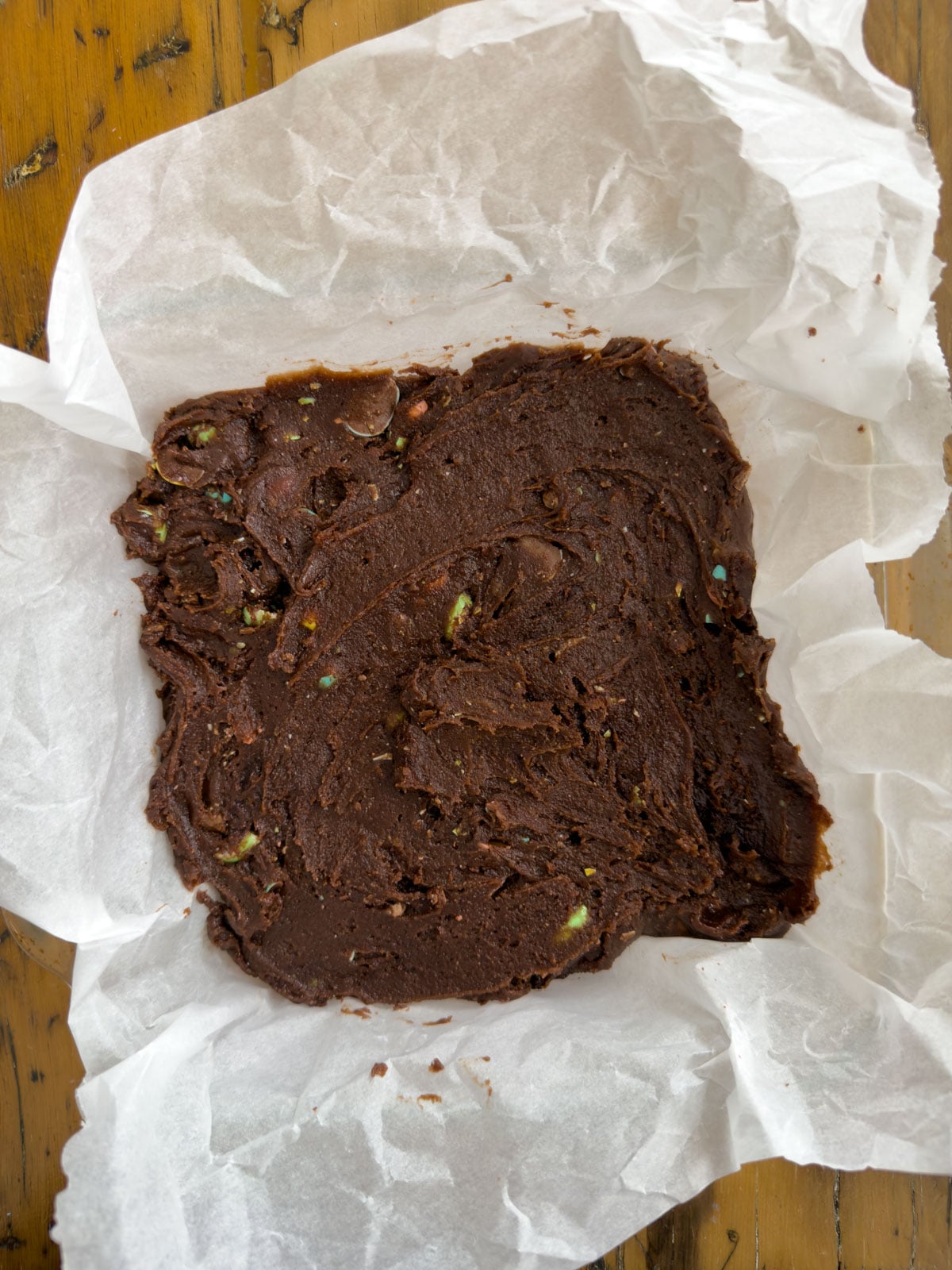 Chocolate brownie batter with crushed Cadbury mini eggs spread evenly in a parchment lined baking pan.