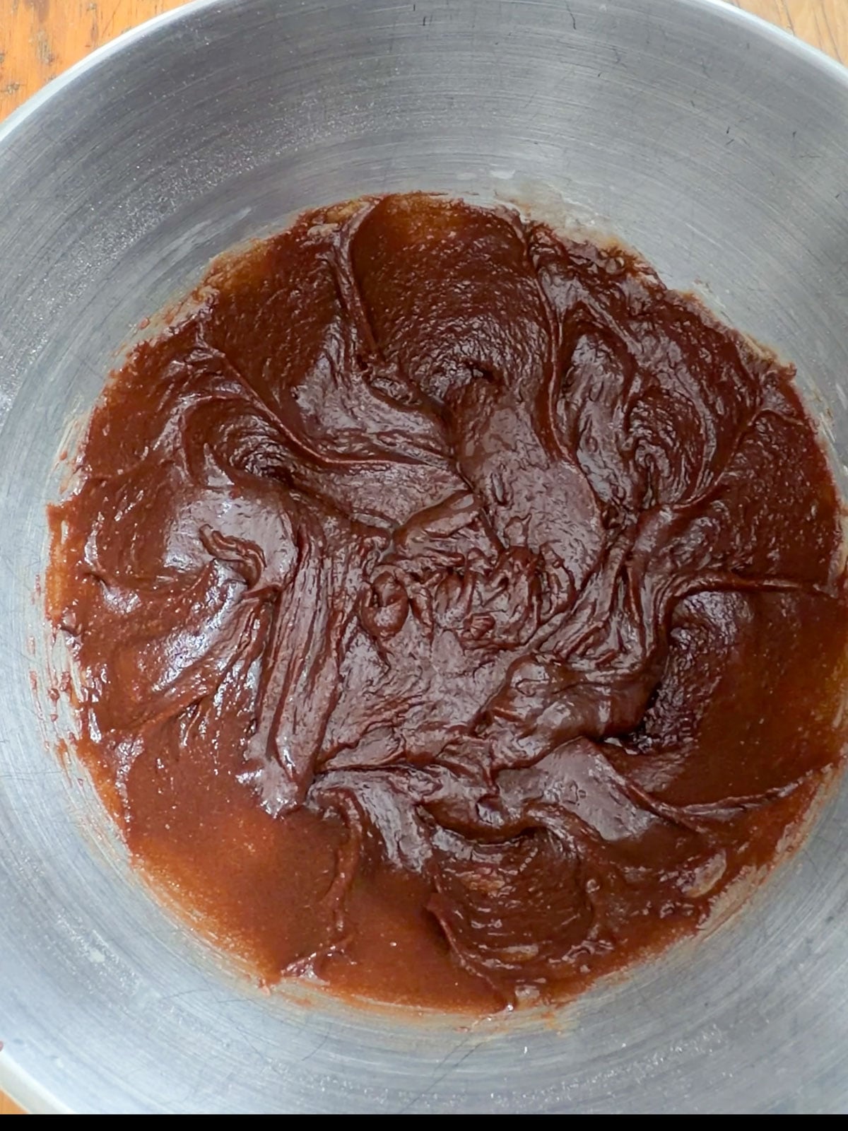 Thick chocolate brownie batter mixed in a large silver mixing bowl.