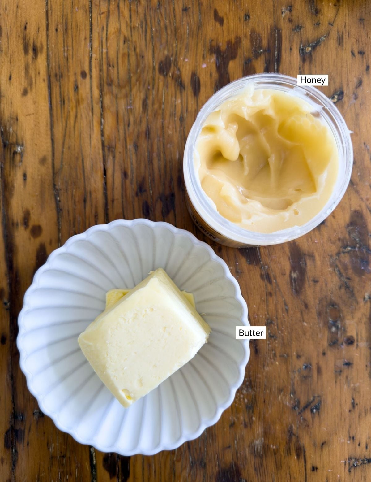 Whipped honey butter in a white ceramic bowl topped with a piece of golden honeycomb and a wooden honey dipper on a rustic wooden table.