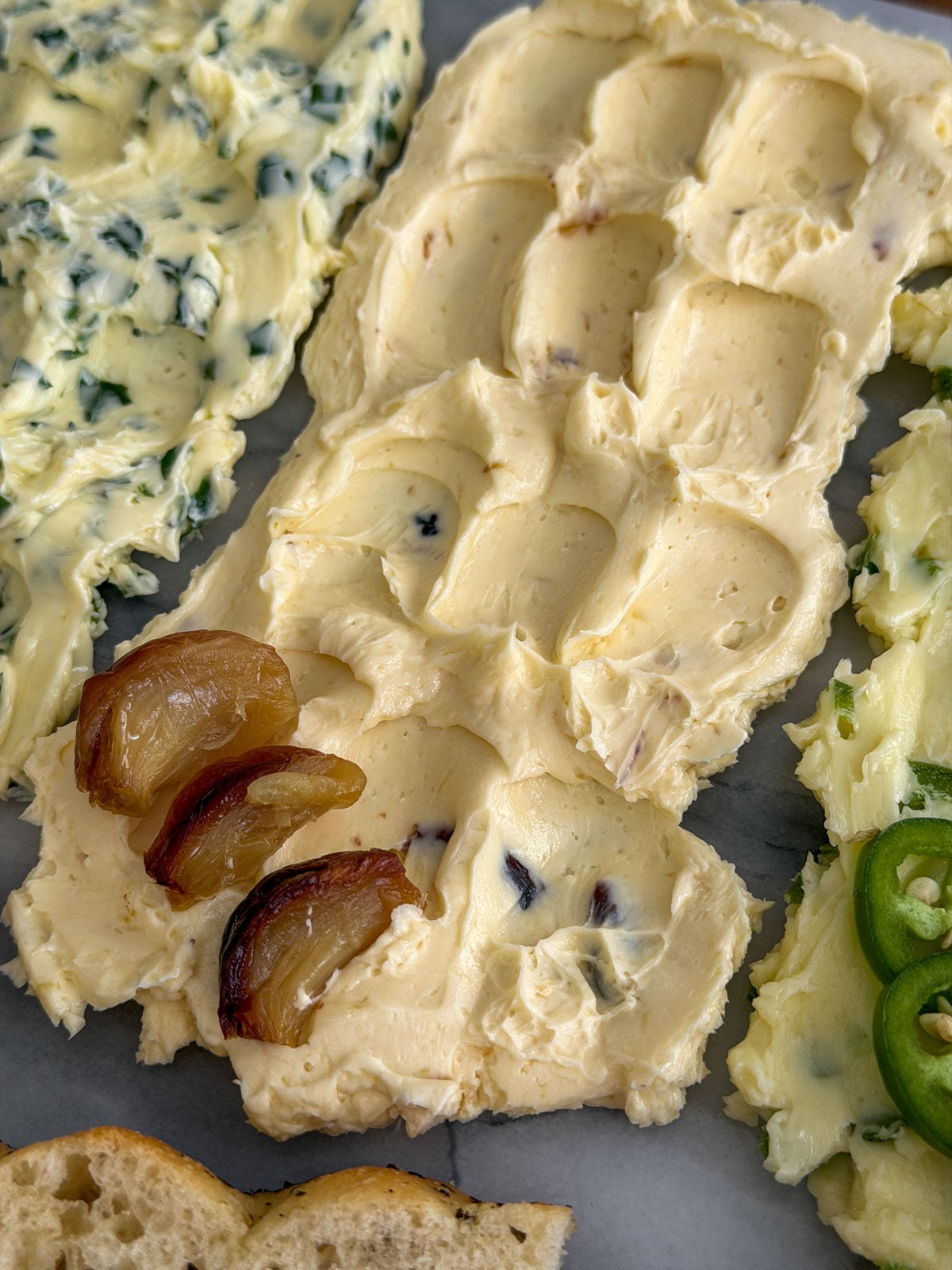 Close up of roasted garlic compound butter spread on a marble board with swooped texture and roasted garlic cloves as garnish.