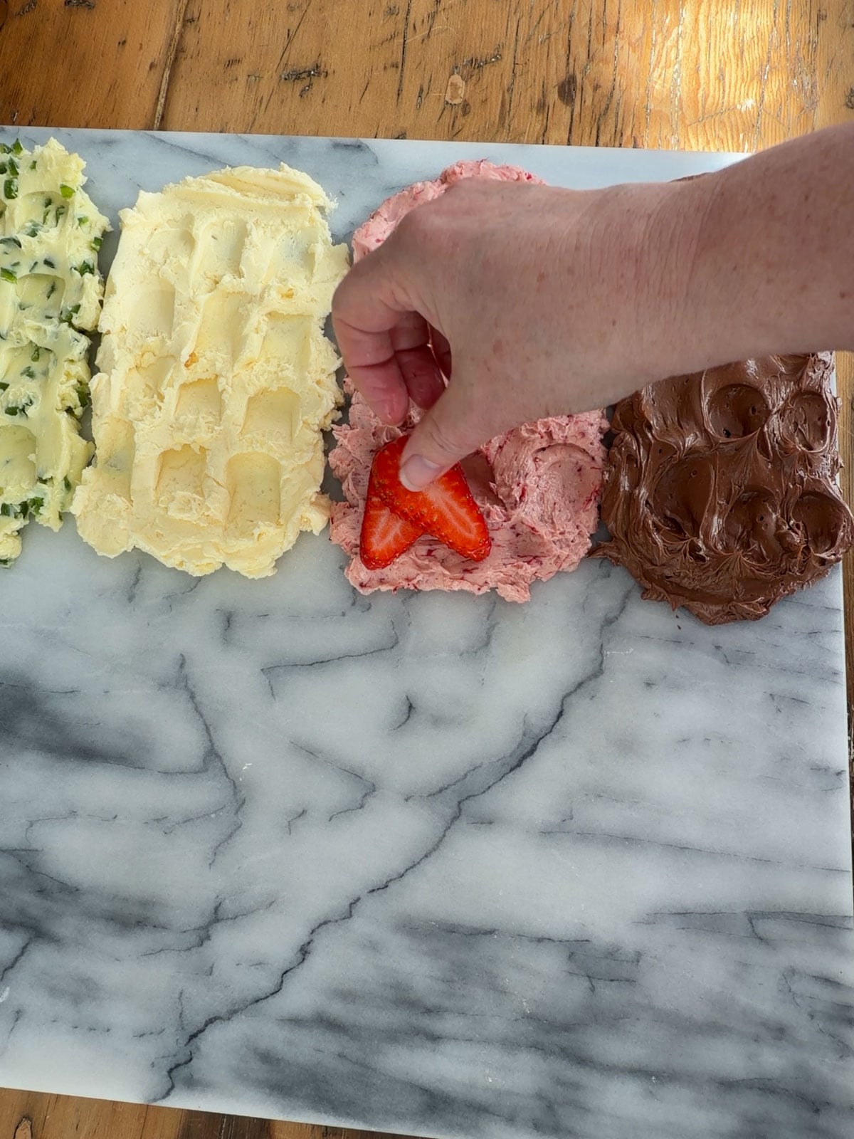 Hand placing a sliced strawberry garnish onto strawberry compound butter on a marble butter board.