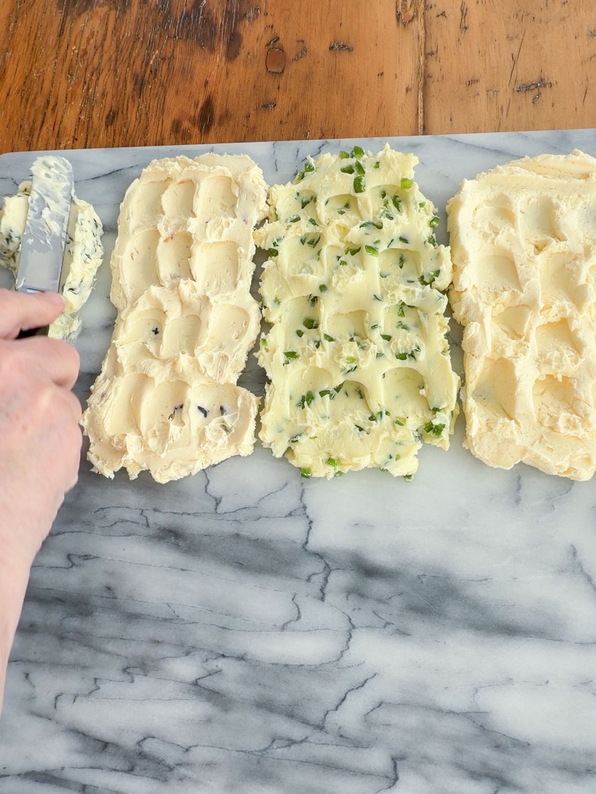 Hand using an offset spatula to spread compound butter onto a marble board in sections.