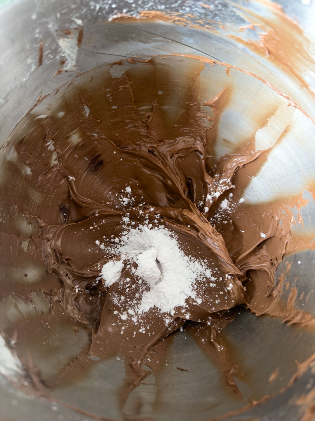  Powdered sugar added to chocolate butter mixture in a stand mixer bowl ready to be incorporated.