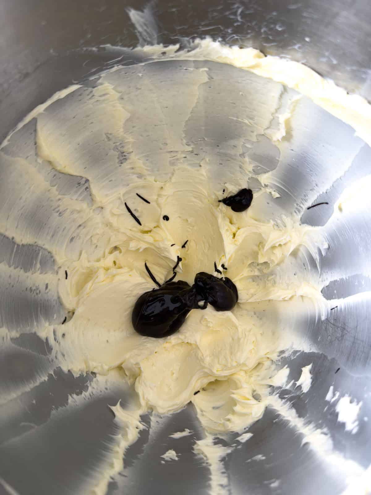 Pale fluffy whipped butter in a stand mixer bowl with cocoa paste beginning to be added.