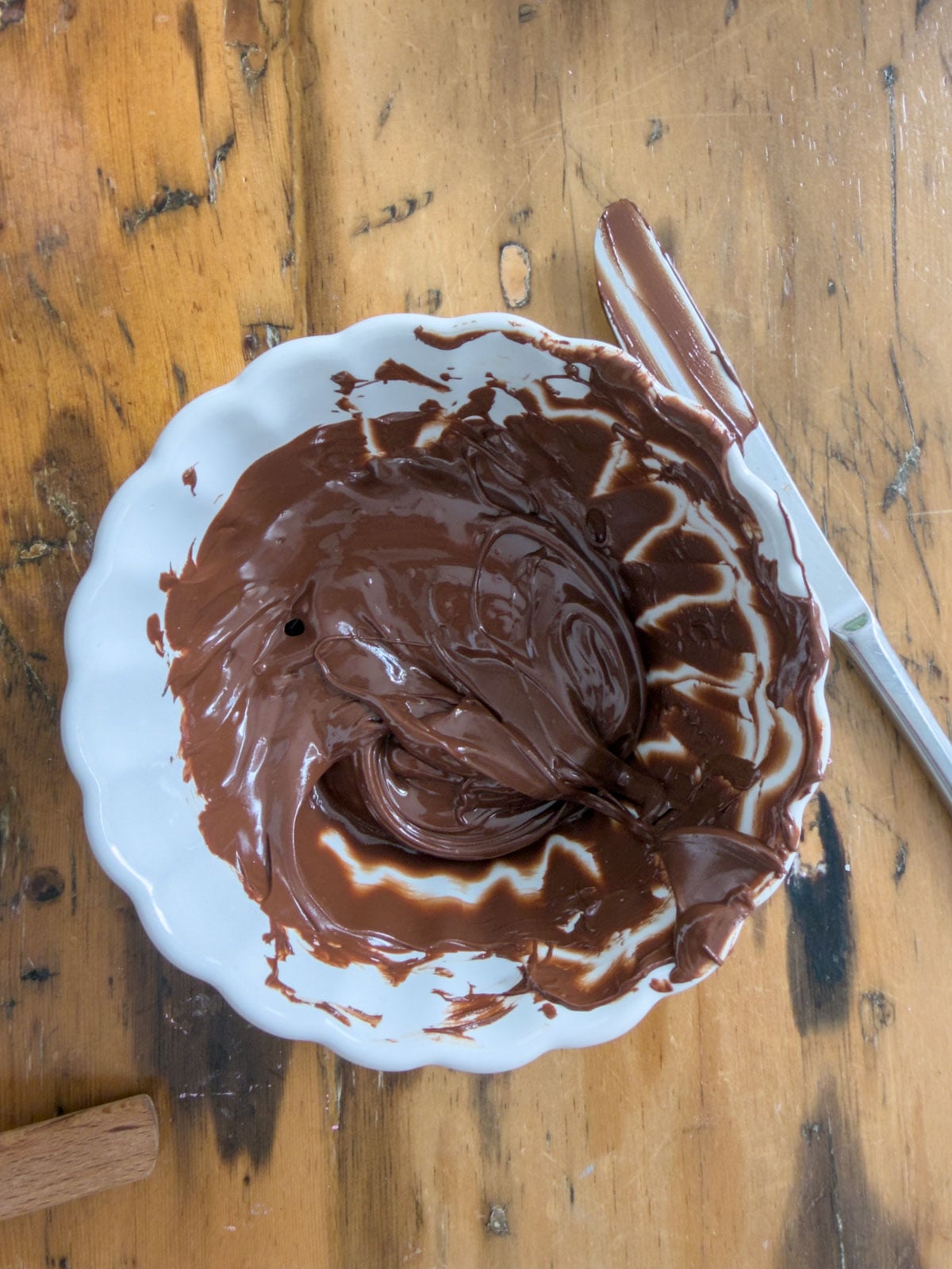 Melted semi-sweet chocolate in a white scalloped bowl on a wooden table.