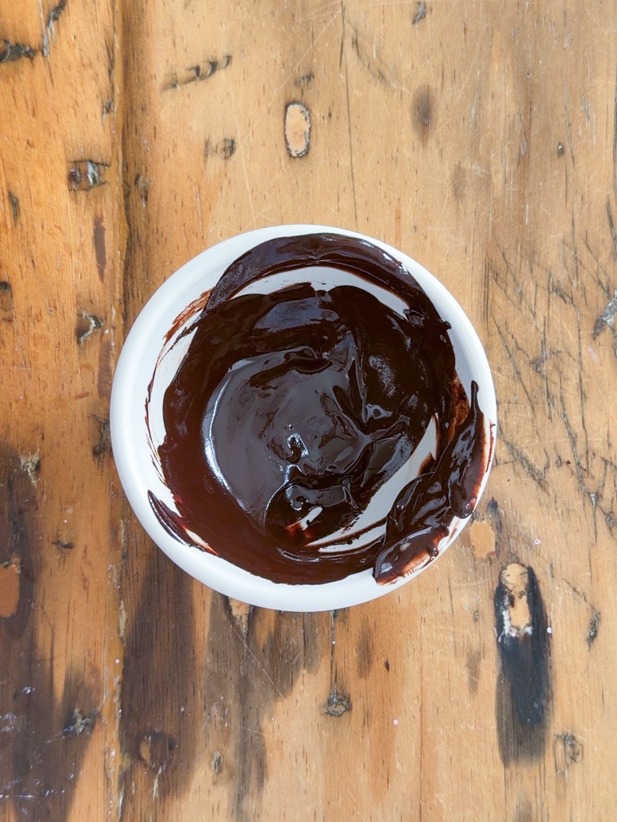 Cocoa powder bloomed in melted butter and stirred into a smooth dark paste in a small white bowl on a wooden table.