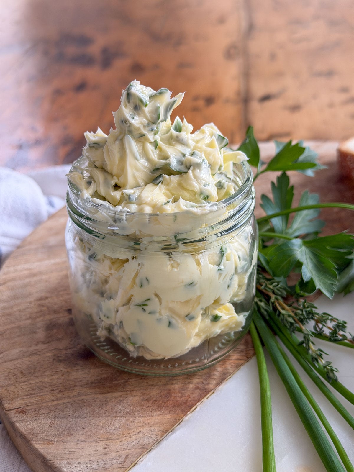 Garlic herb compound butter piled high in a glass jar showing fresh herb flecks throughout, with parsley and chives alongside