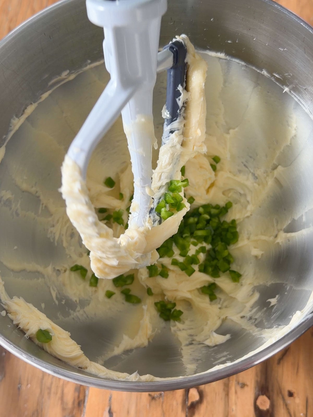 Finely diced jalapeno pieces being added to whipped butter in a stand mixer bowl, showing the beginning of mixing jalapeno honey butter.