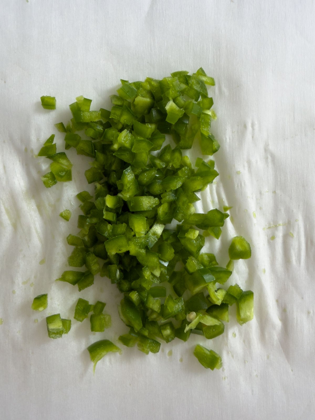 Finely diced fresh jalapeno pieces spread on a white paper towel, ready to be added to jalapeno honey butter.