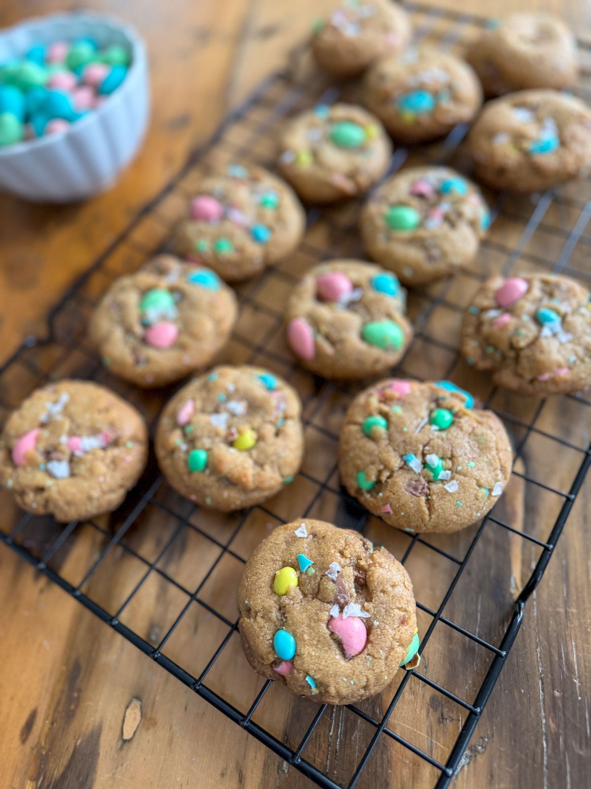 Cadbury mini egg cookies with brown butter cooling on a wire rack with flaky sea salt on top.