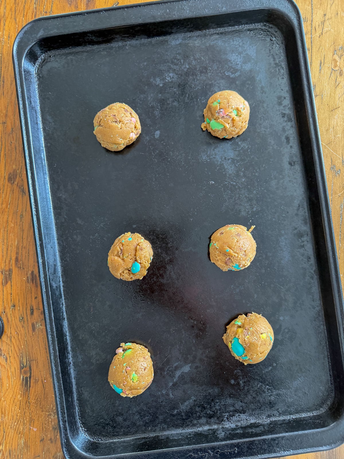 Cadbury mini egg cookie dough balls spaced apart on a dark baking sheet ready to go into the oven.