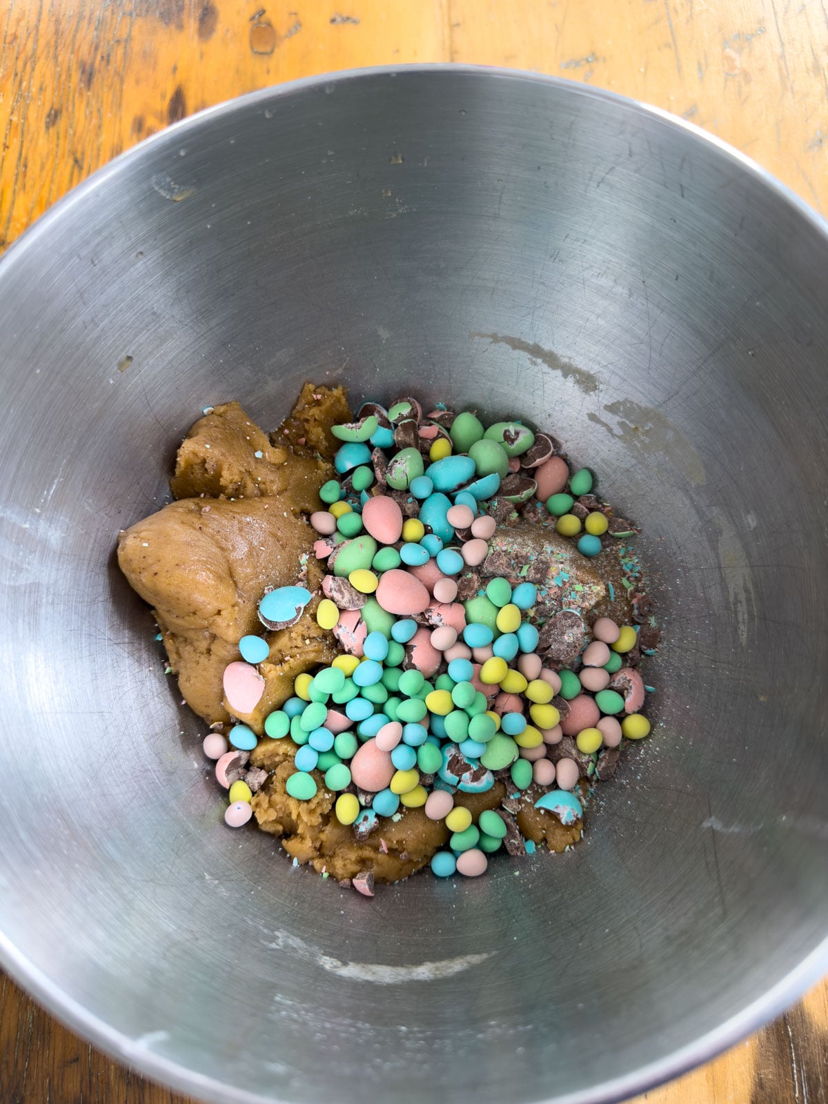 Crushed Cadbury mini eggs and micro mini eggs being added to brown butter cookie dough in a silver mixing bowl.