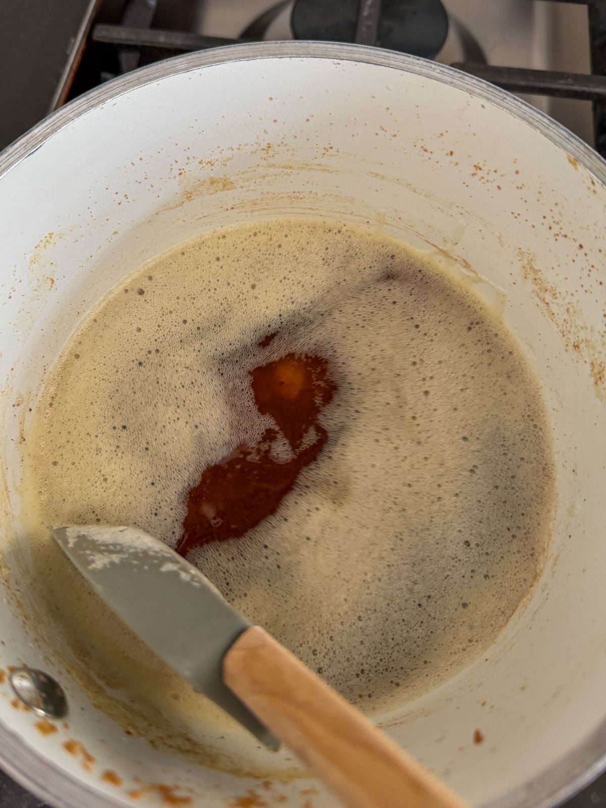Butter foaming and browning in a white saucepan on the stovetop with golden brown milk solids beginning to form.