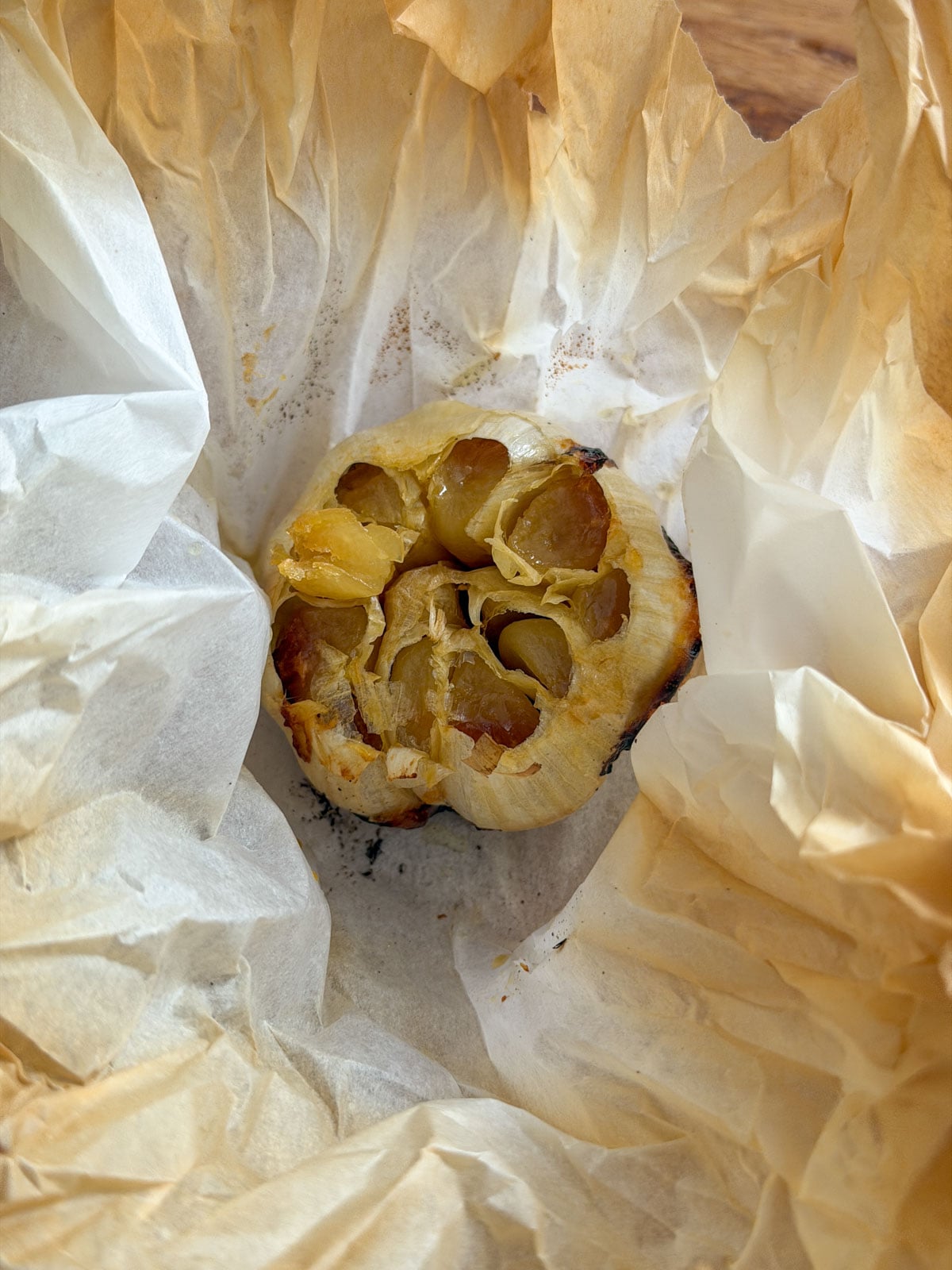 Roasted garlic head with caramelized golden cloves unwrapped from parchment paper after baking.