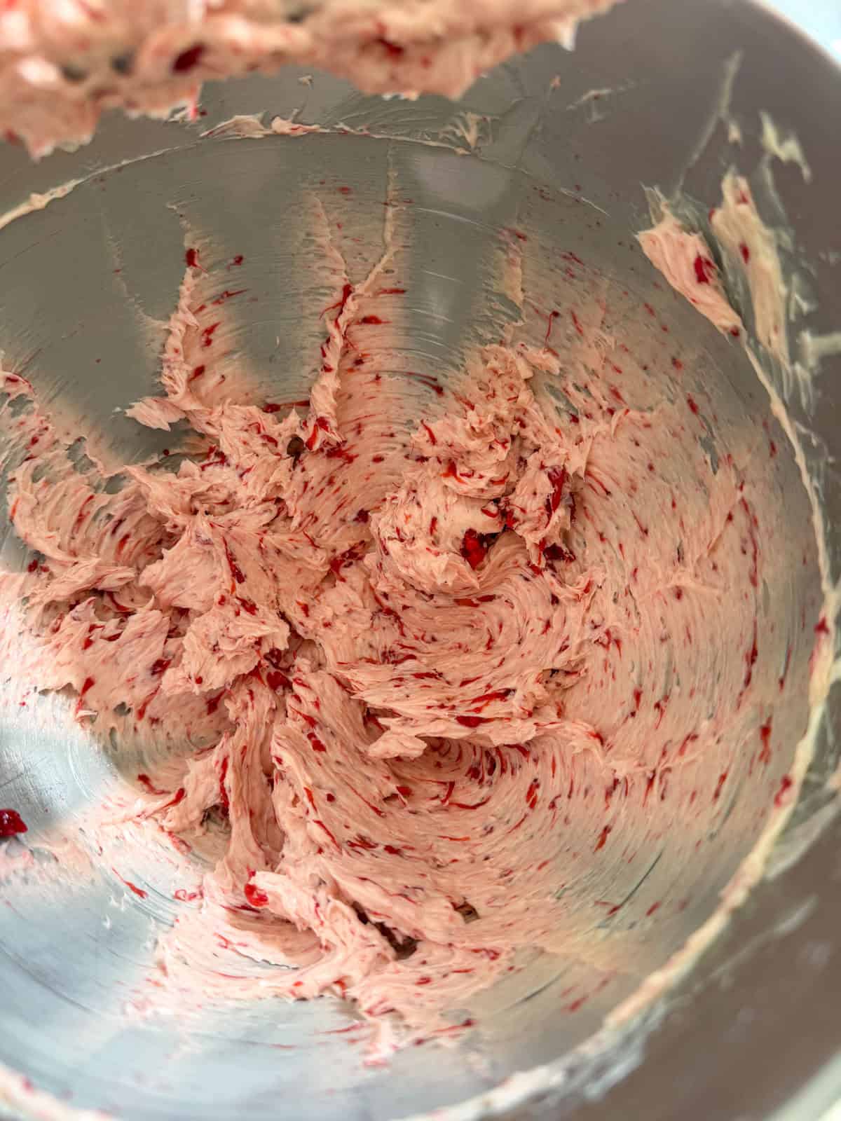 Pink strawberry butter swirled in a stainless steel stand mixer bowl after the strawberry reduction has been fully incorporated.