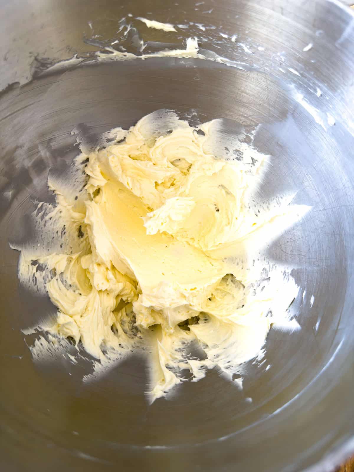Pale whipped butter in a stainless steel stand mixer bowl after being beaten until light and fluffy.