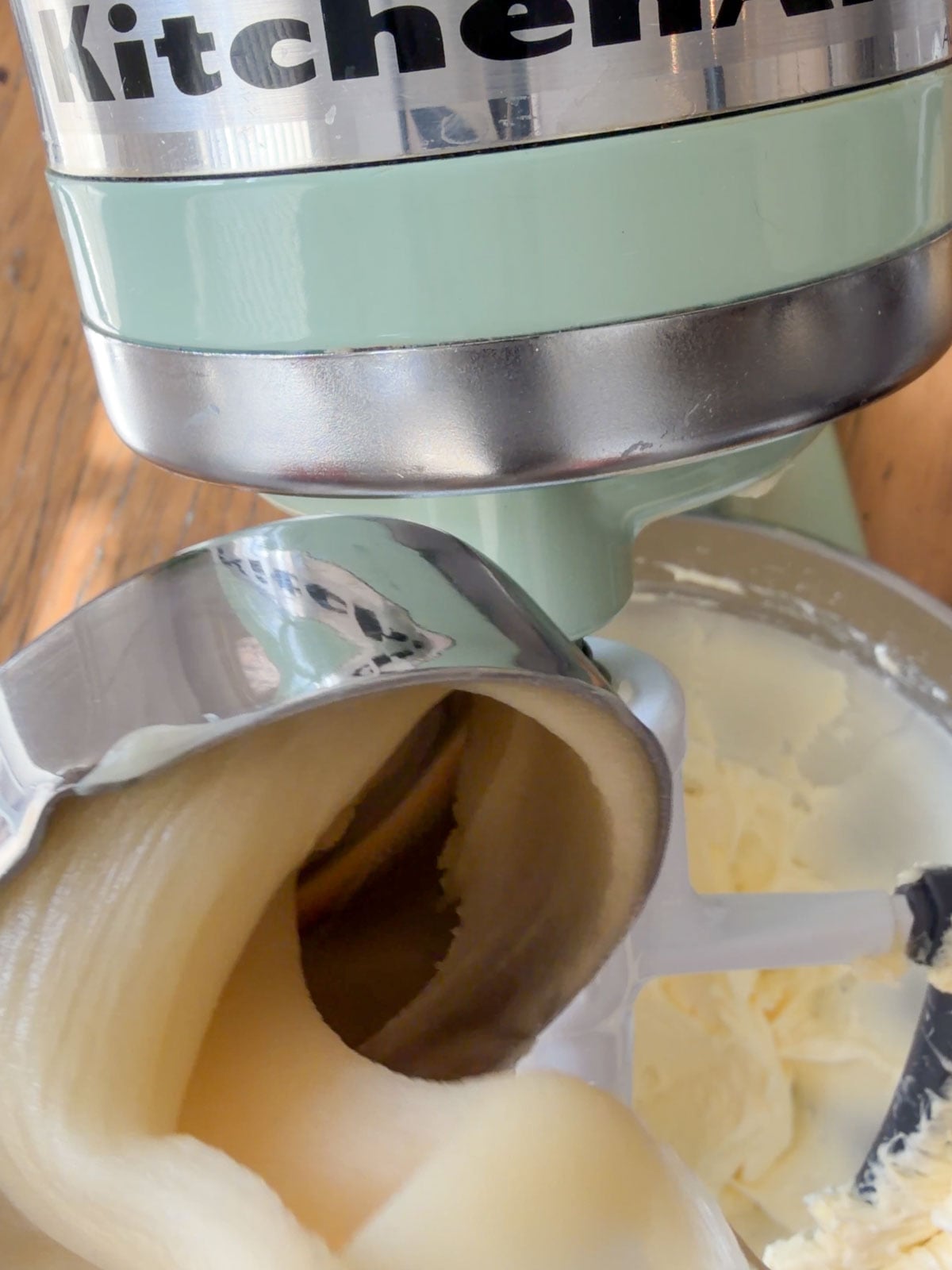 Creamed honey being added to whipped butter in the bowl of a mint green KitchenAid stand mixer.