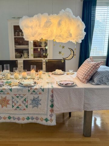 Breakfast for dinner party table styled like a bed with star quilt tablecloth, gingham pillows, and cloud installation above.