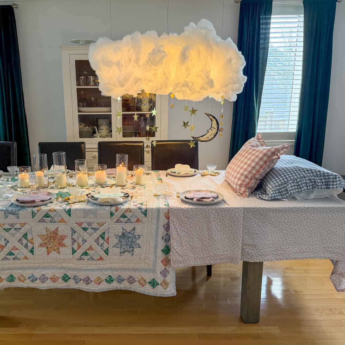 Breakfast for dinner party table styled like a bed with star quilt tablecloth, gingham pillows, and cloud installation above.