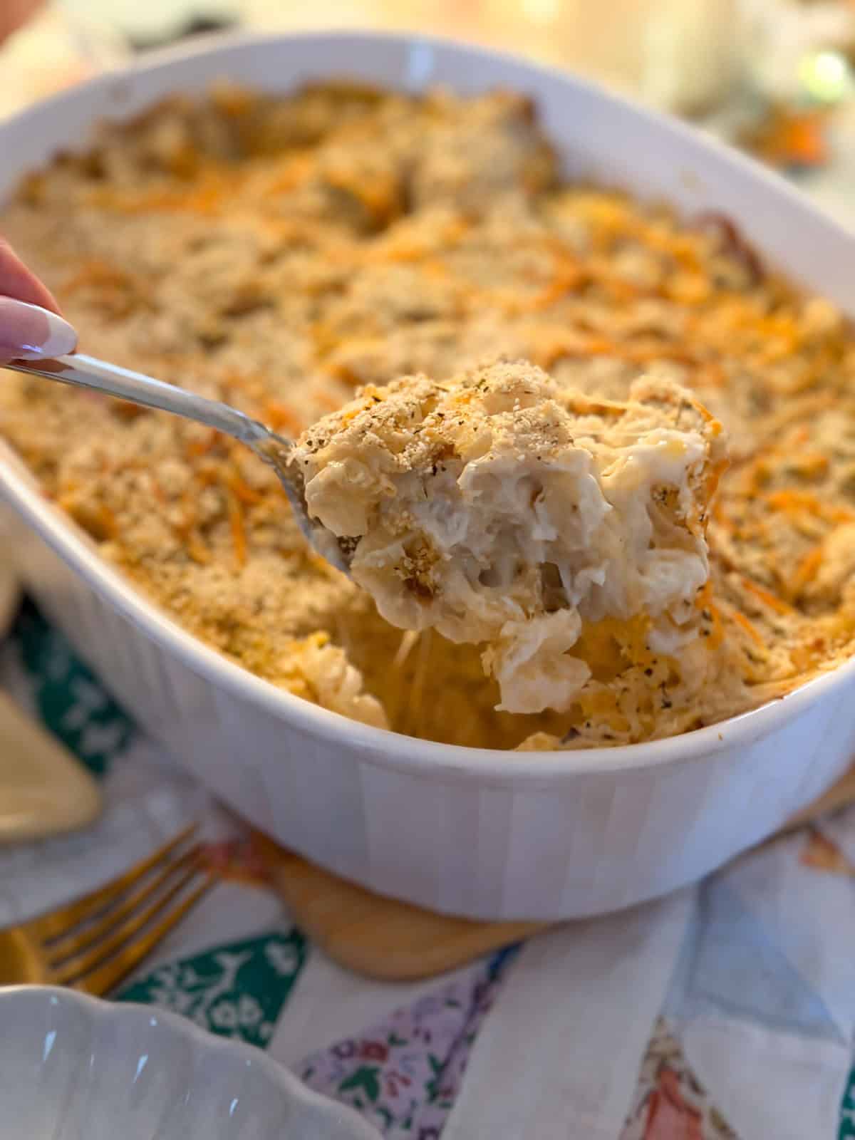 Hashbrown casserole with golden breadcrumb topping being scooped from a white oval baking dish.