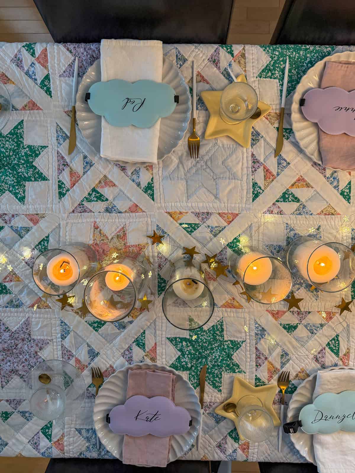 Overhead view of breakfast for dinner party place settings with personalized cloud shaped sleep mask name cards in mint, lavender, and pink on a vintage star quilt.