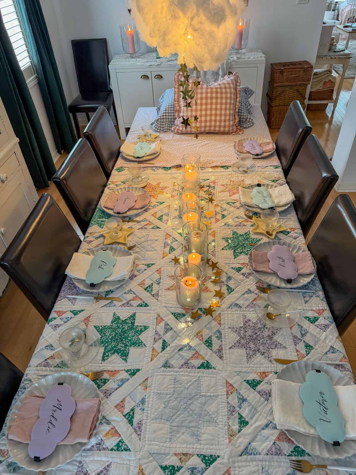 Full dining room decorated for a breakfast for dinner party with DIY cloud installation, vintage quilt tablecloth, gingham ruffle pillow headboard, and floral gallery wall.