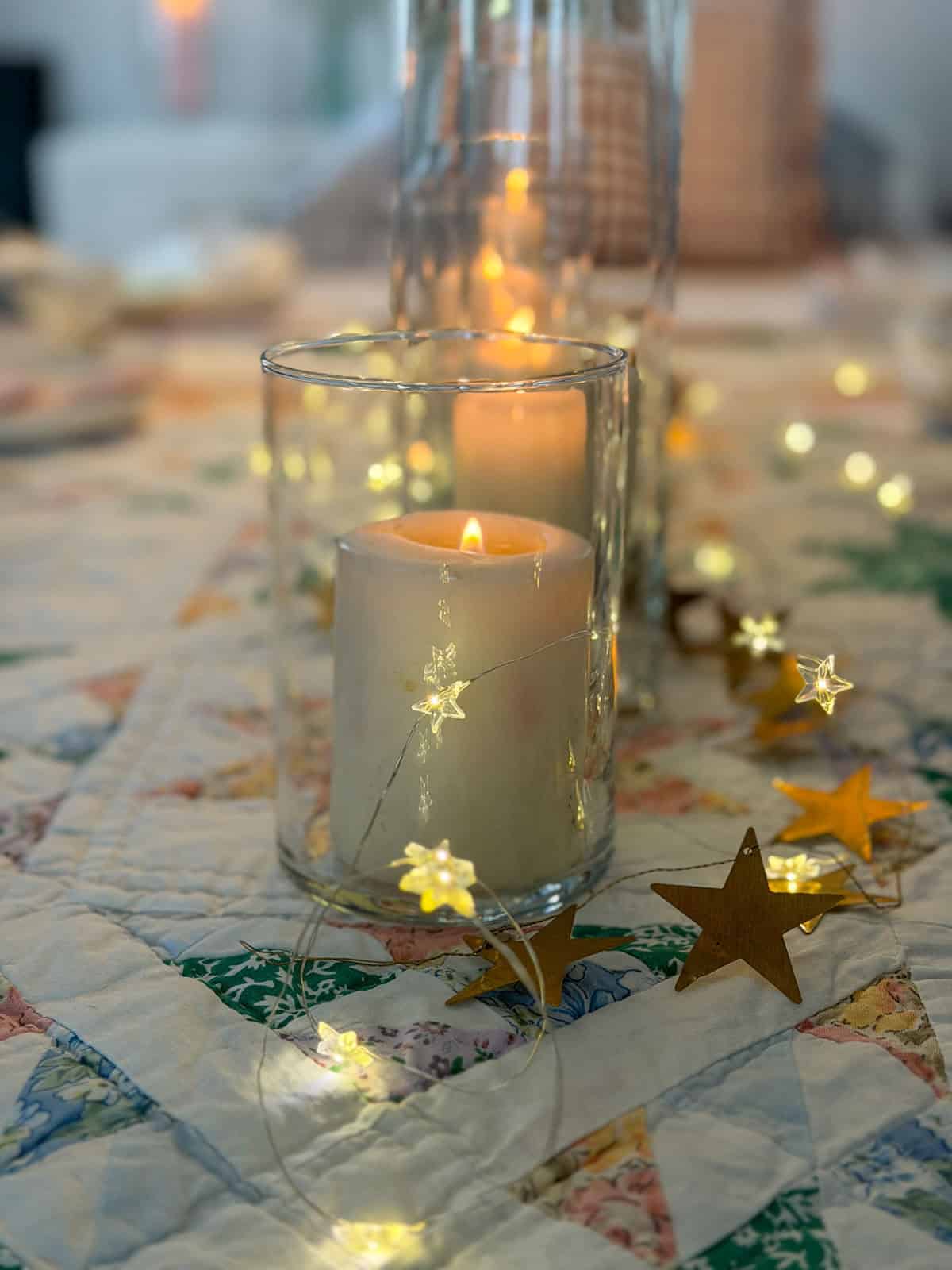 Pillar candle in glass cylinder vase with gold star garland and star fairy lights on a vintage star pattern quilt tablecloth.