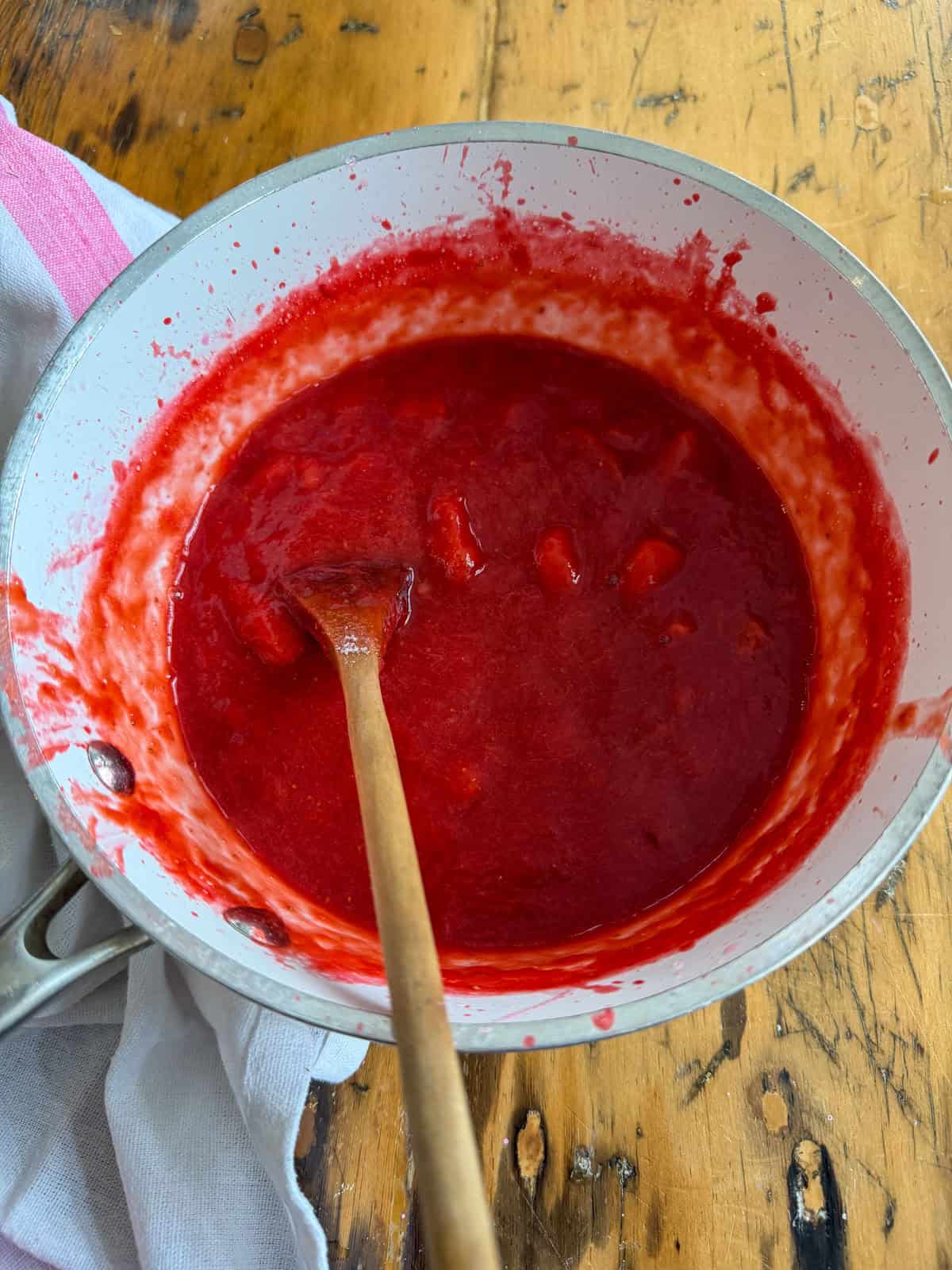 Finished strawberry rhubarb compote in a white saucepan stirred with a wooden spoon.