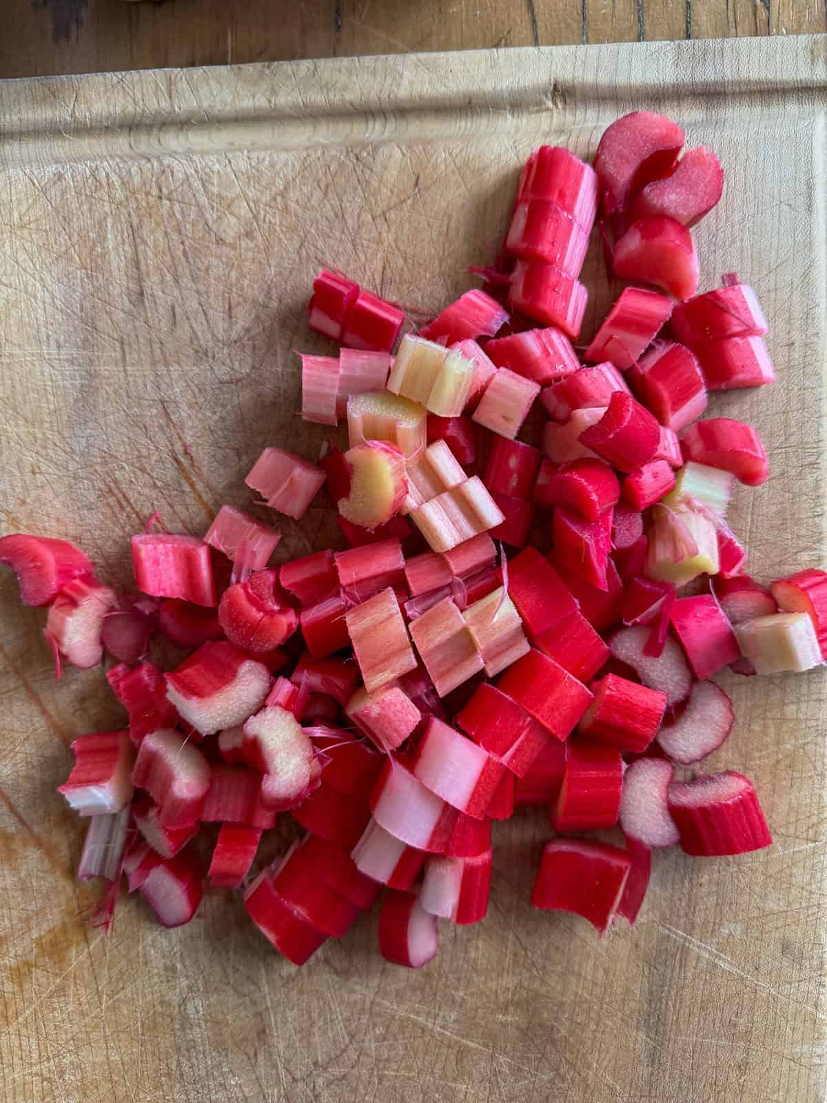 Fresh rhubarb stalks chopped into small uniform pieces on a wooden cutting board.