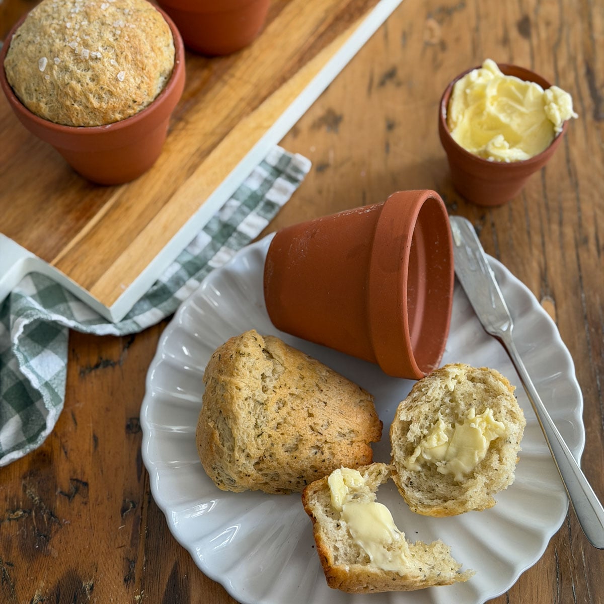 Flower pot bread torn open on a white plate with butter, alongside terracotta pots on a wooden serving board.
