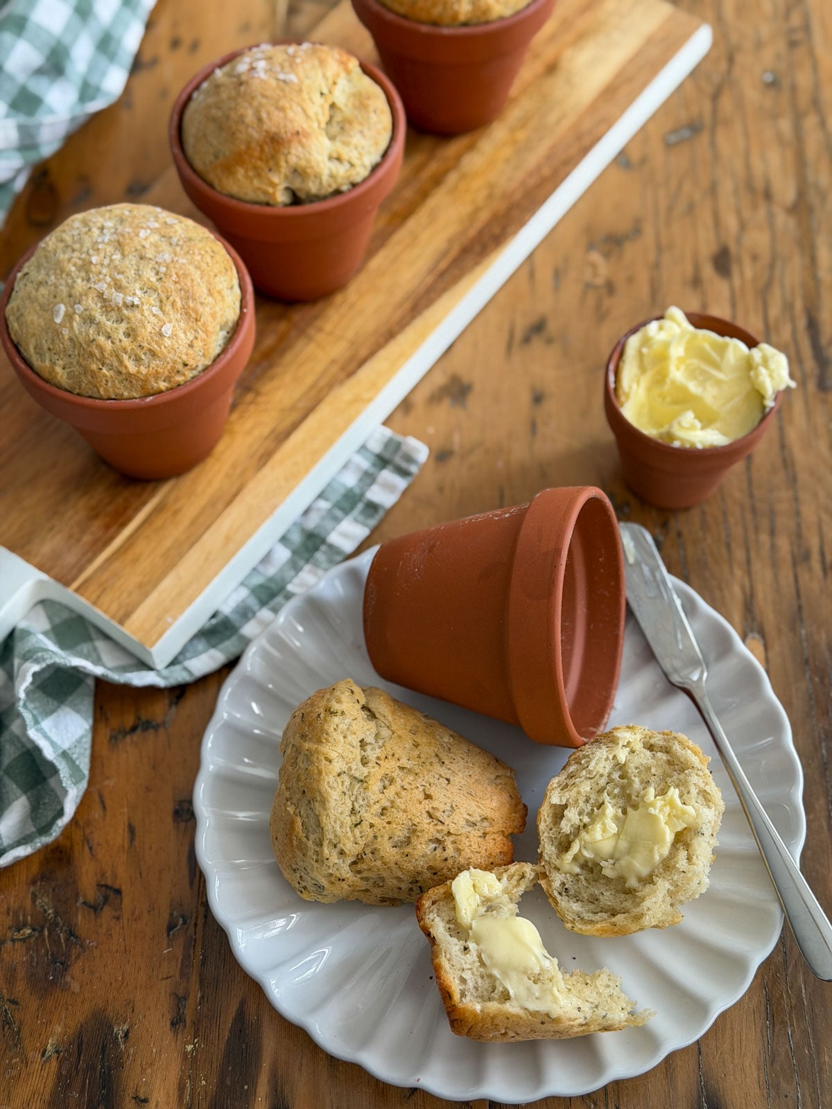 Individual flower pot bread loaves served on a white plate with butter, alongside terracotta pots on a wooden serving board.