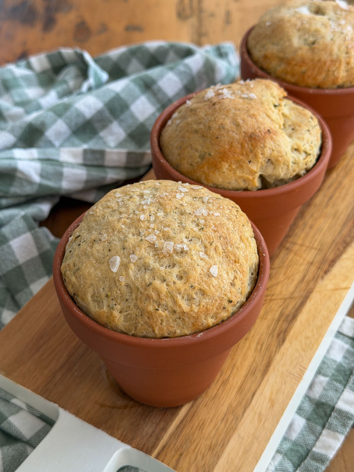 Freshly baked flower pot herb bread with golden crust and flaky sea salt in terracotta pots.