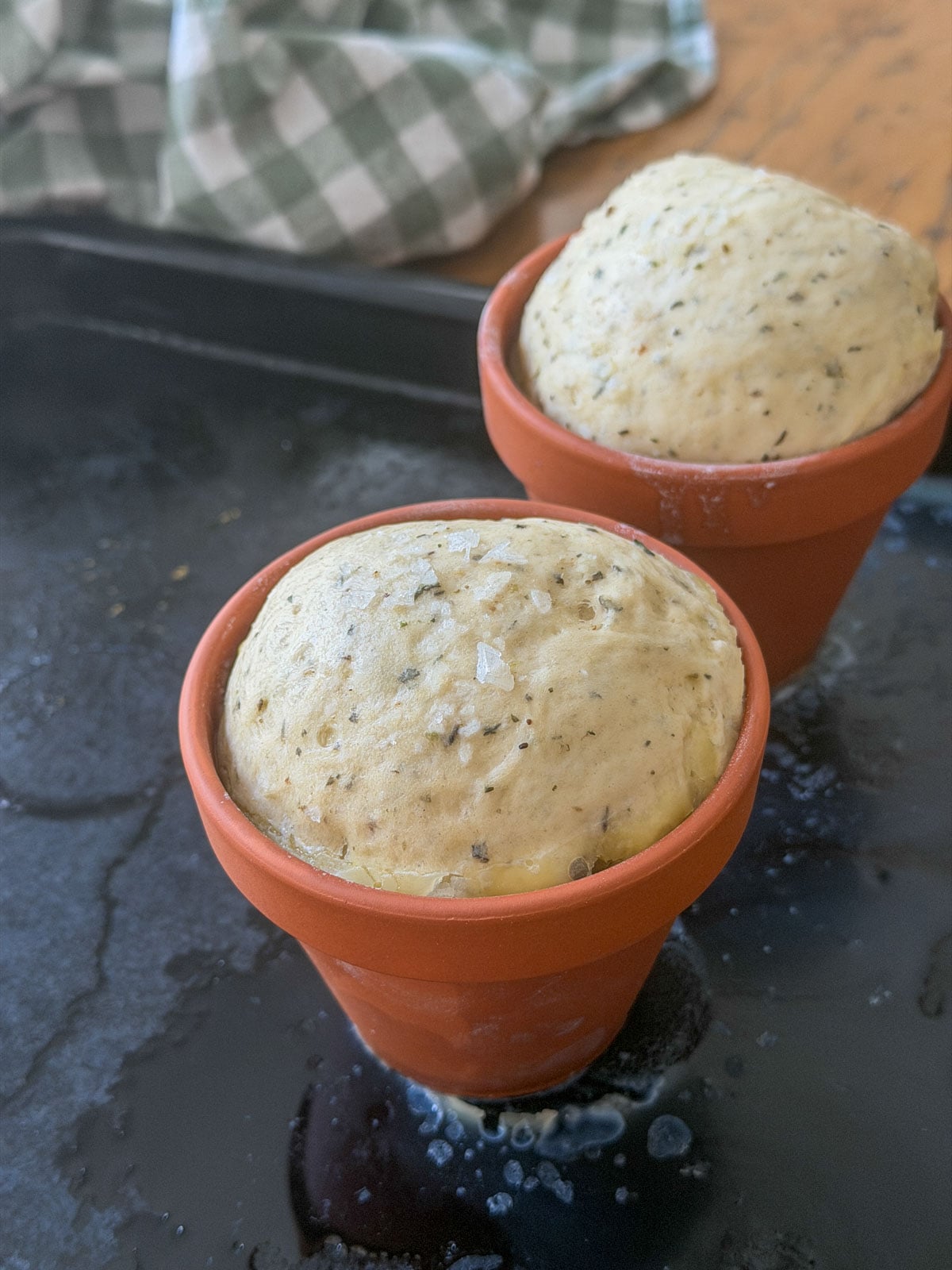 Herb bread dough risen above the rim of terracotta flower pots, brushed with butter and sprinkled with flaky sea salt.