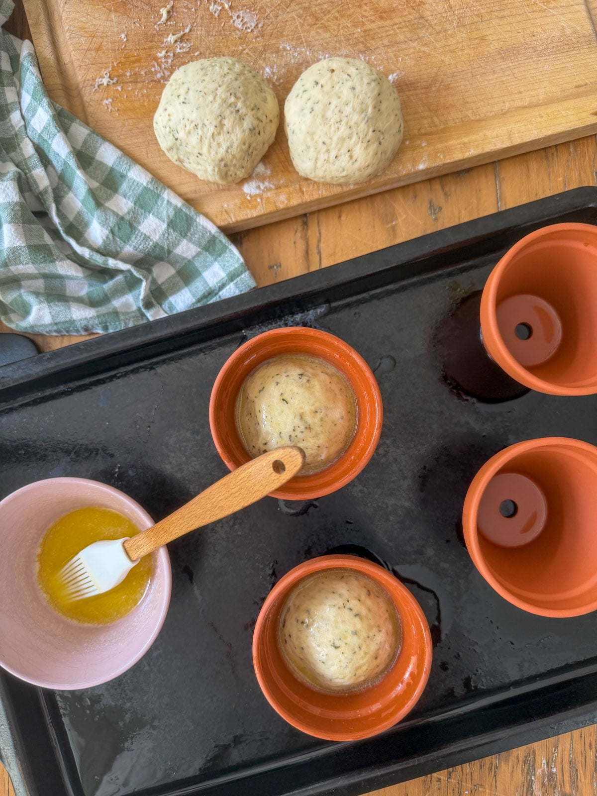Herb bread dough balls shaped and placed into buttered terracotta pots ready for second rise.