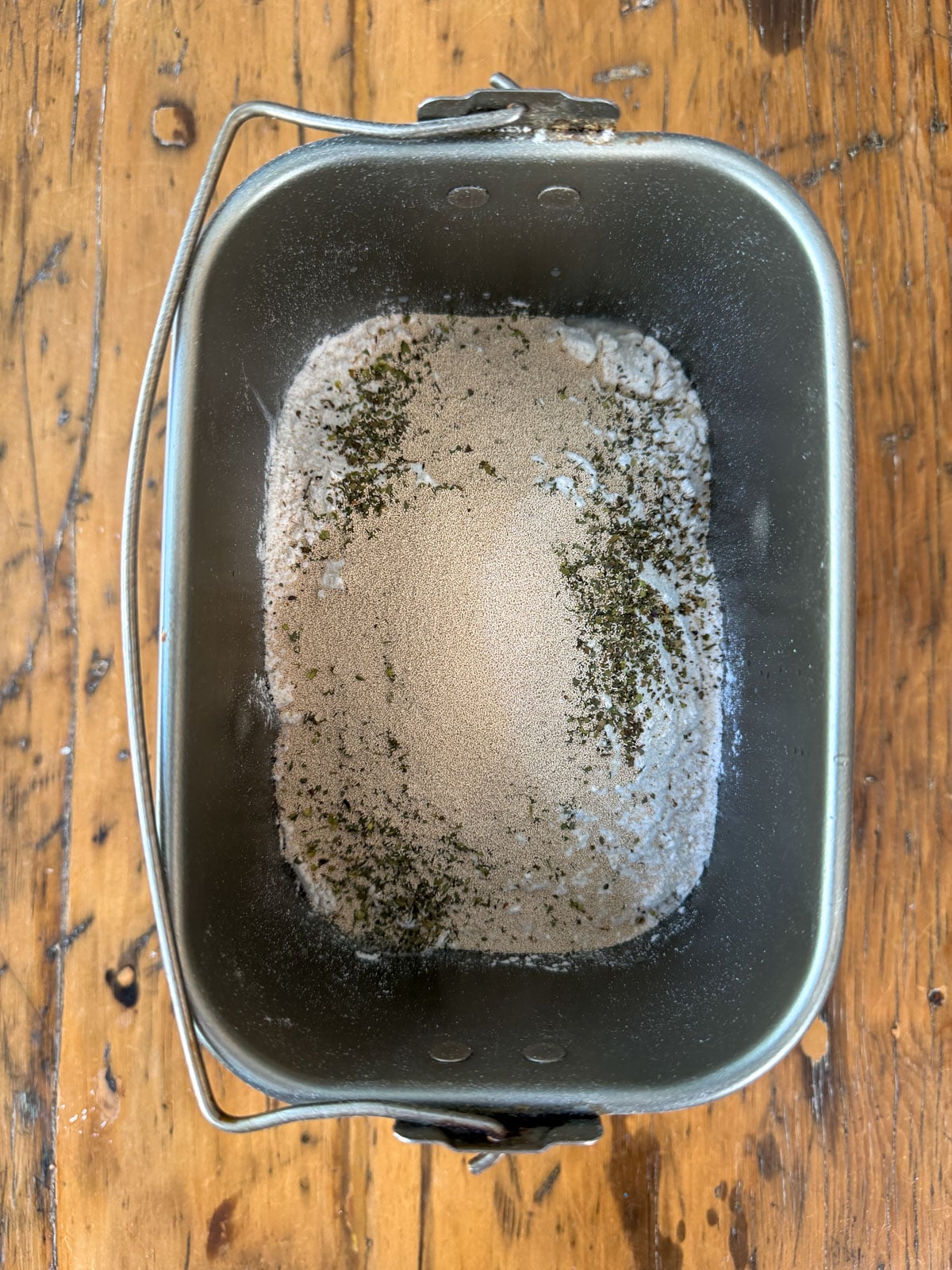 Bread machine pan with flour, yeast, and Italian seasoning ready to mix.