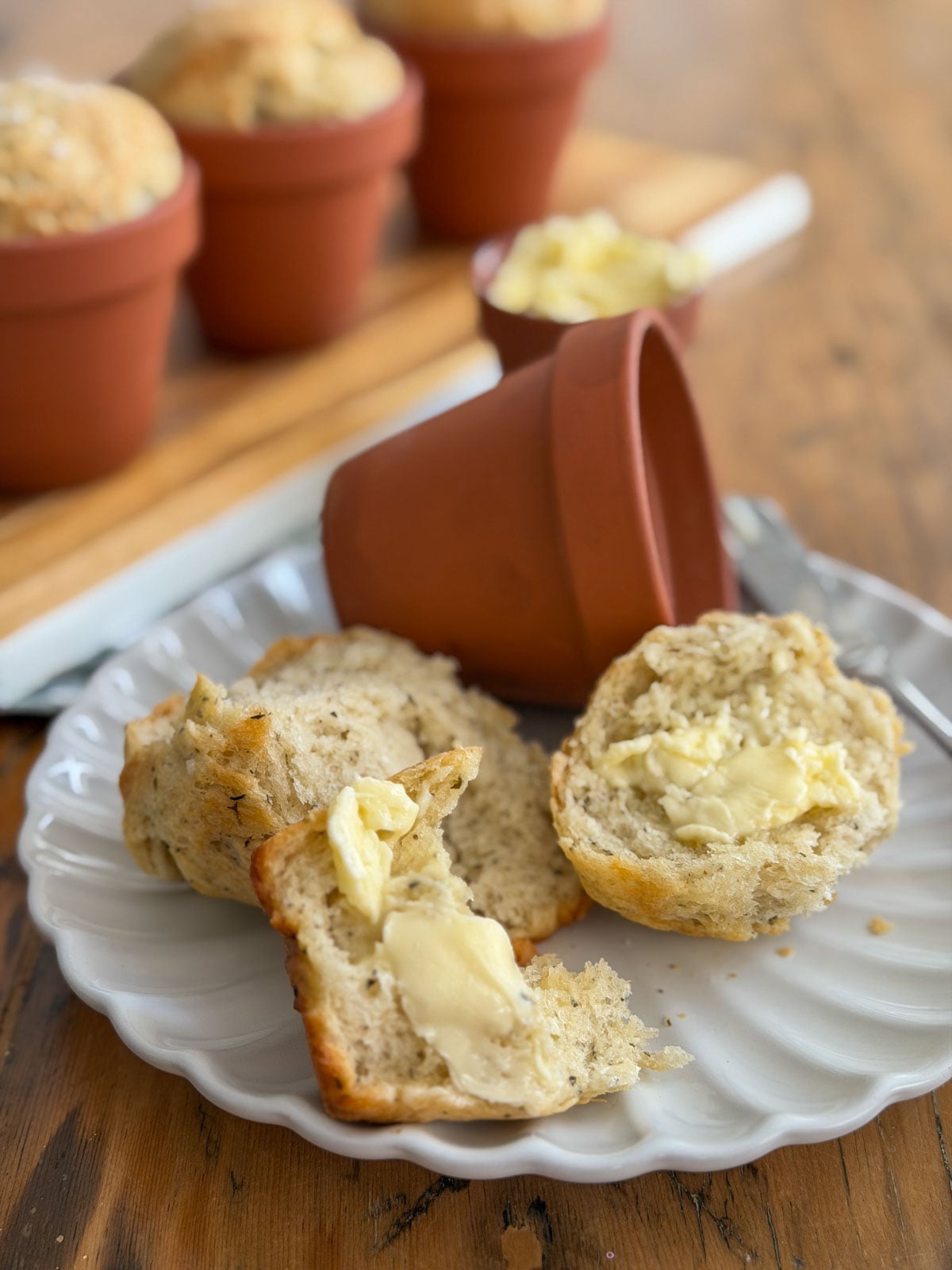 Flower pot bread torn open on a white plate showing soft herb crumb with melted butter.