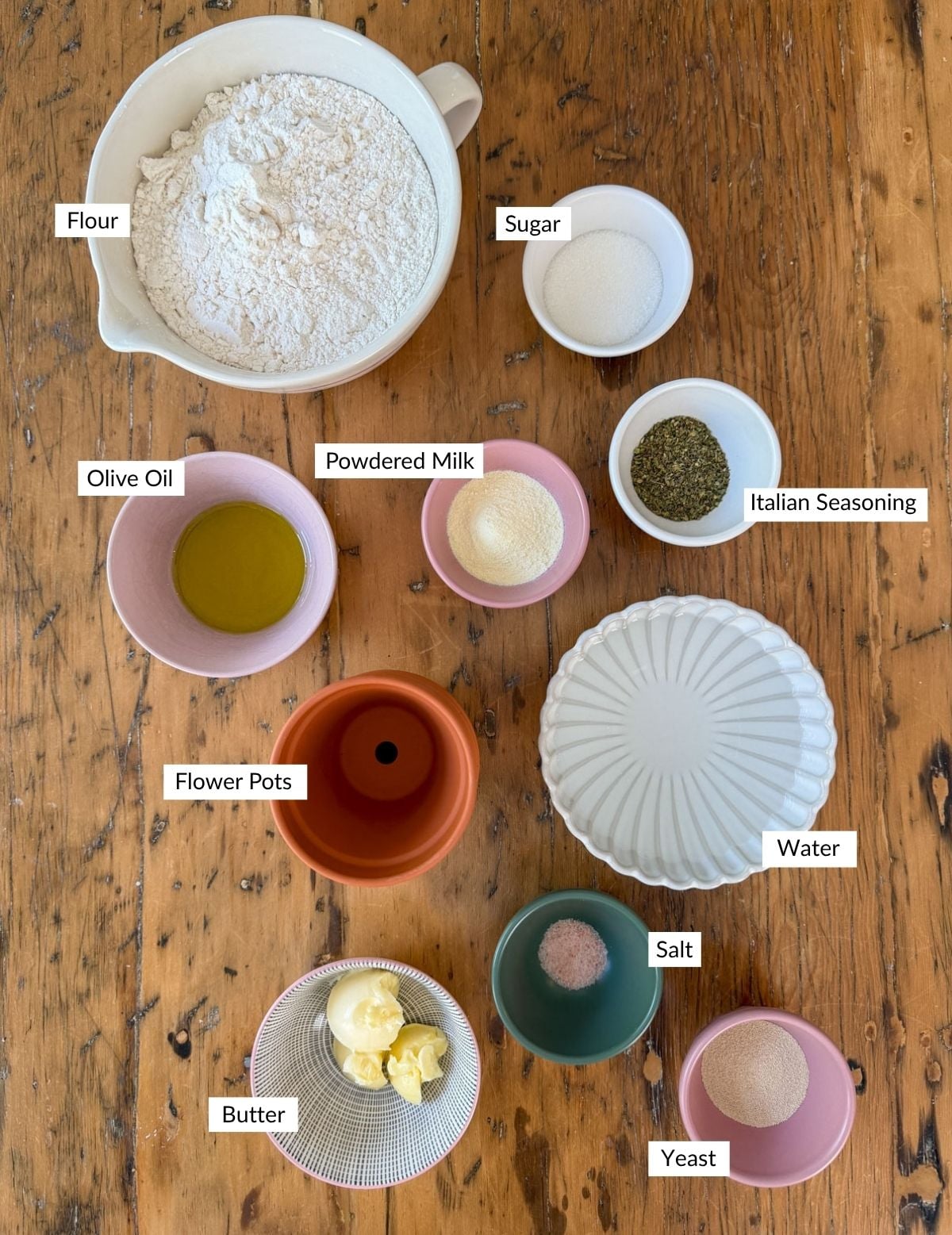 Flower pot bread ingredients including flour, sugar, powdered milk, Italian seasoning, olive oil, butter, salt, yeast, water, and a terracotta flower pot.