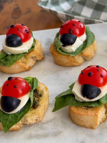 Ladybug caprese bruschetta on a basil leaf with mozzarella, olive, and balsamic glaze spots.