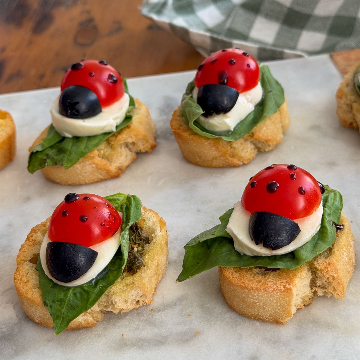 Ladybug caprese bruschetta on a basil leaf with mozzarella, olive, and balsamic glaze spots.