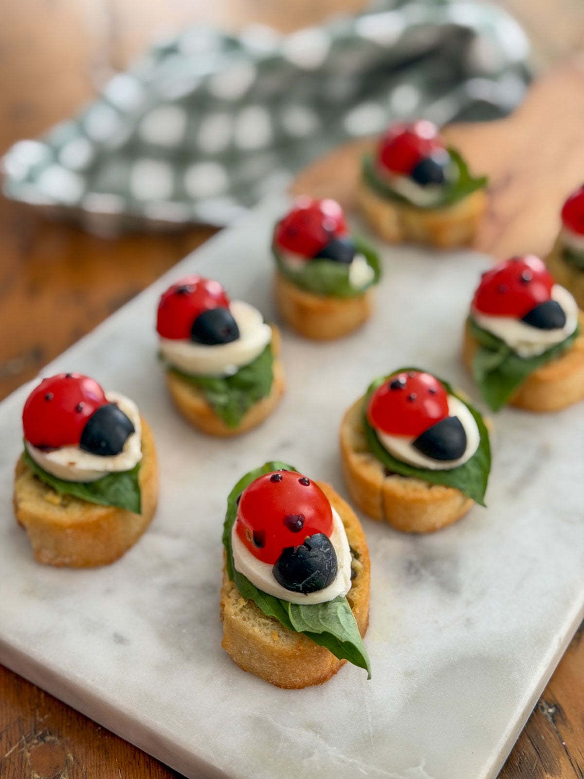 Ladybug caprese bruschetta arranged in rows on a marble and wood serving board.