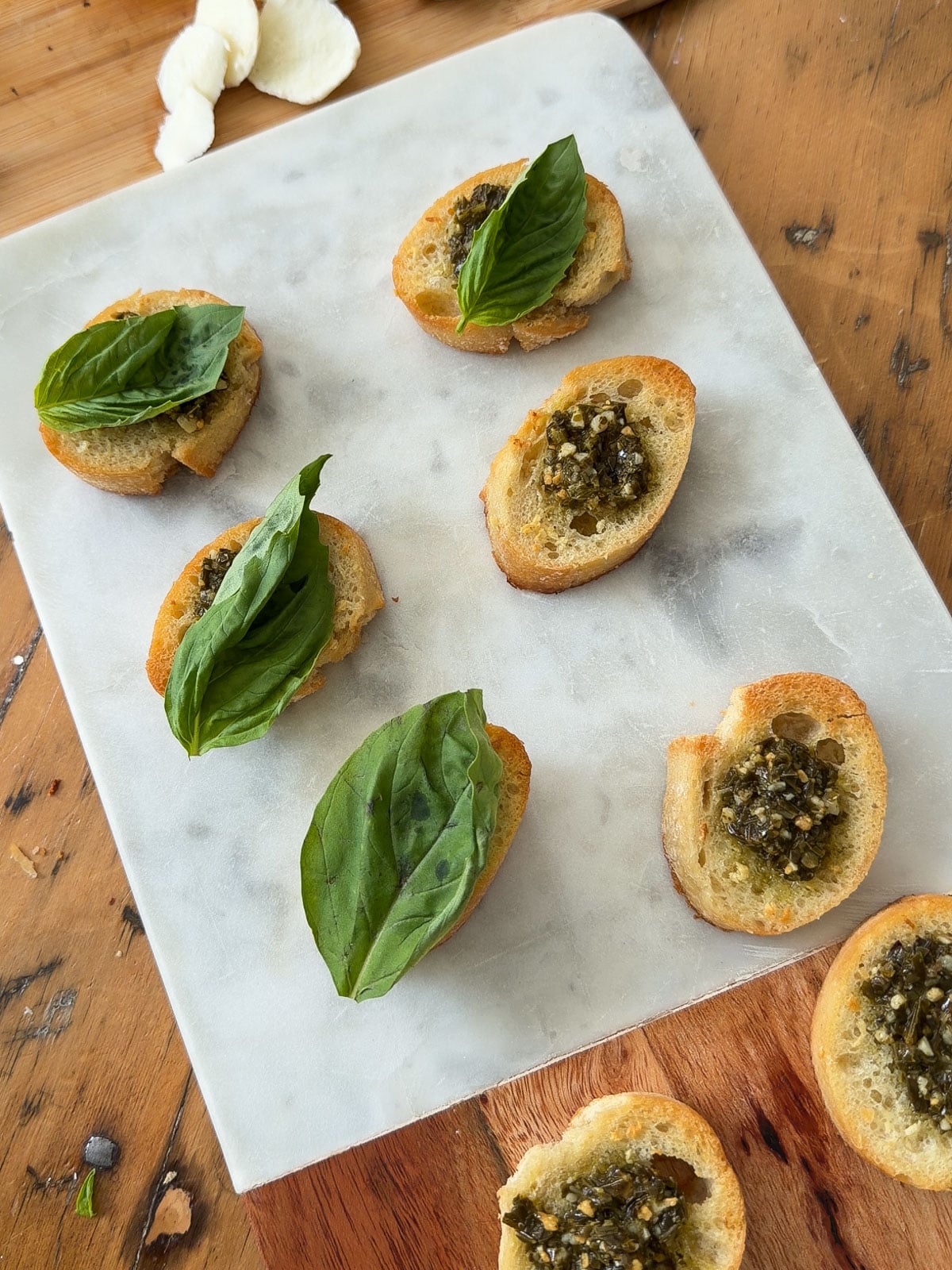 Garlic butter crostini topped with pesto, mozzarella, and fresh basil leaves.