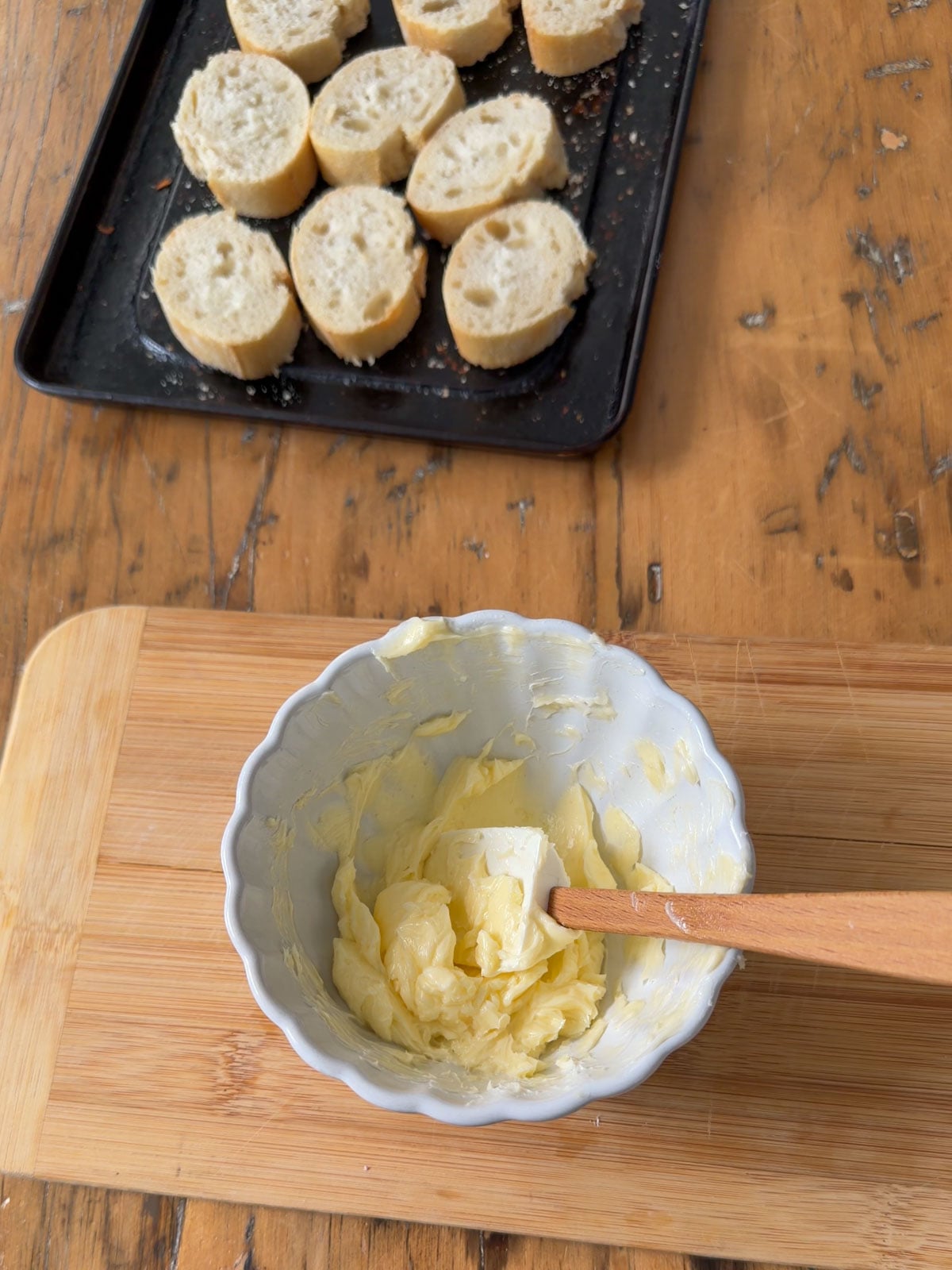 Garlic butter mixed in a bowl beside sliced baguette ready for toasting.
