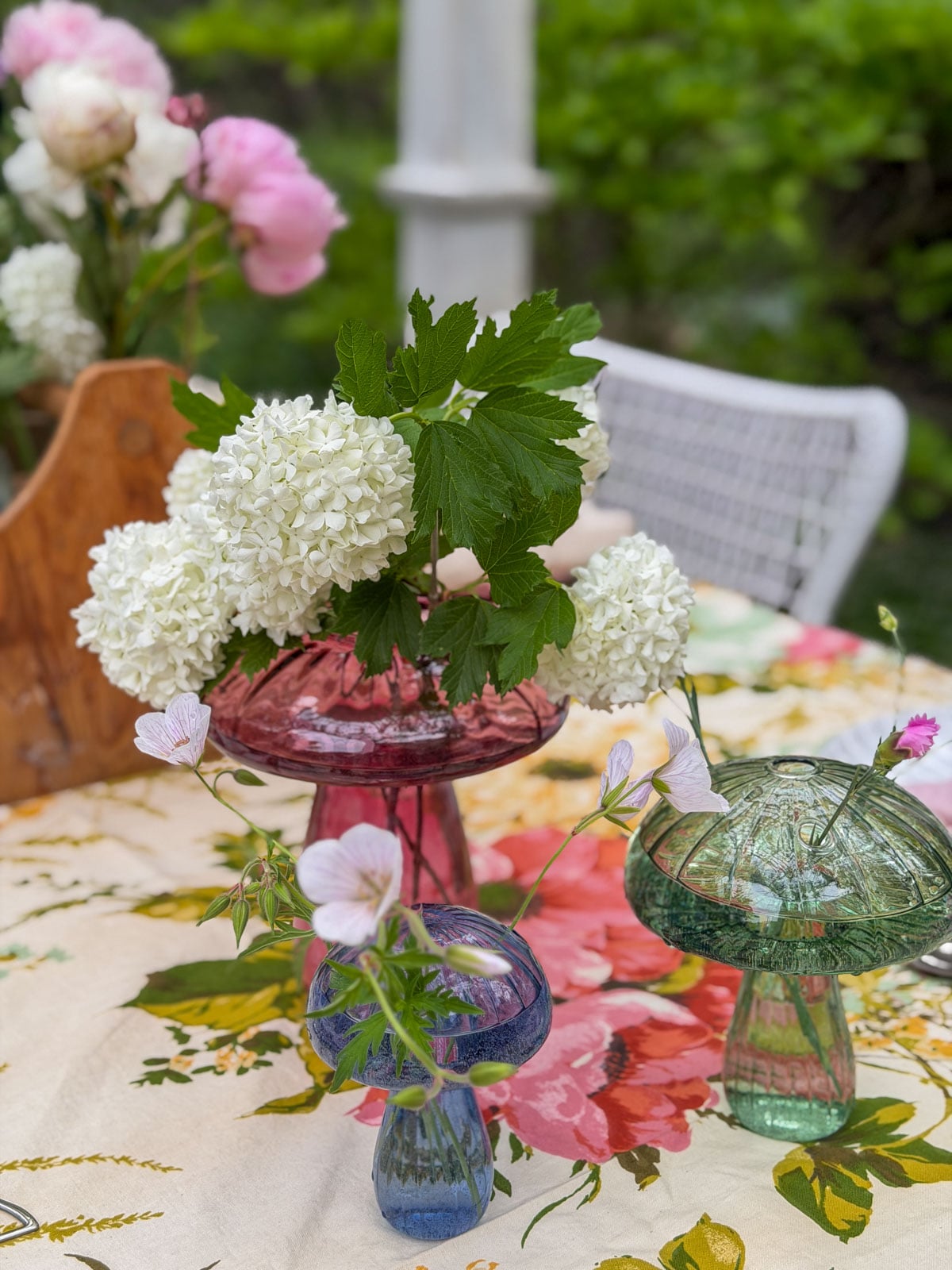 Glass mushroom vases grouped together holding fresh garden flowers on garden party table.