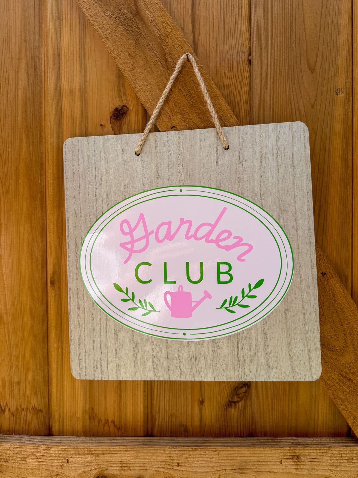 Garden Club sign with pink script and green oval logo hanging on wooden barn door.