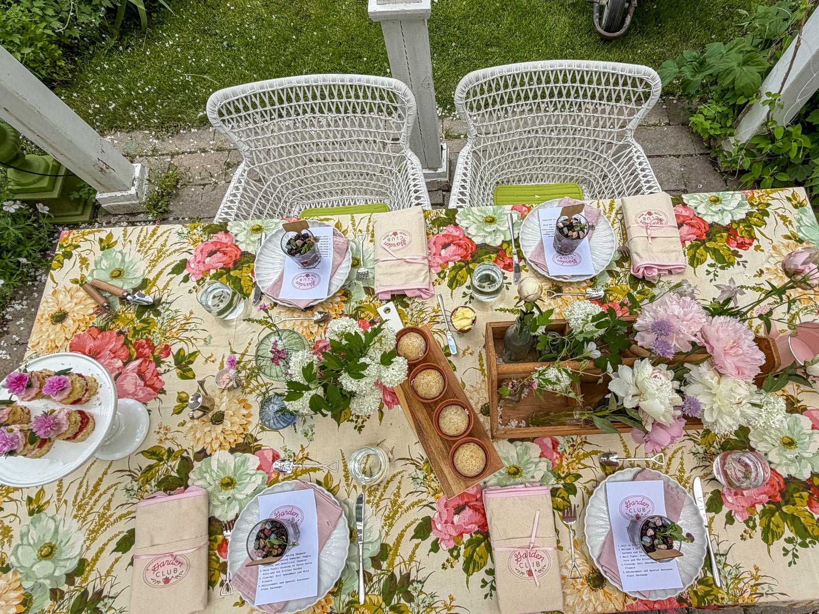 Garden party place setting with dirt pudding placecard, individual sparkling rosé bottle, and wooden flower caddy filled with pink peonies and white hydrangeas on floral tablecloth.